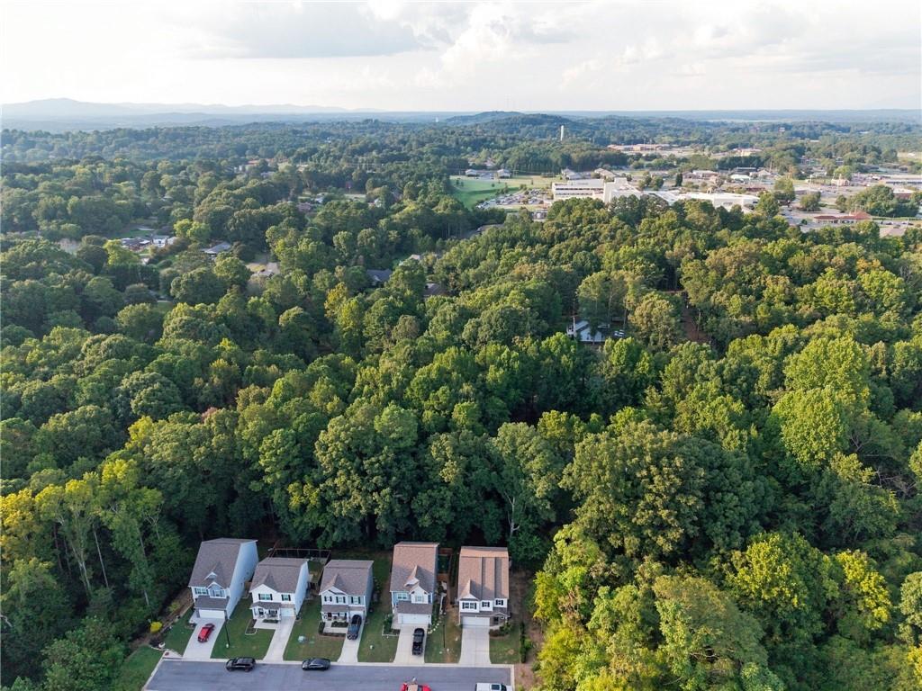 Aerial view of homes bordering dense woods, with a town and distant mountains beyond.