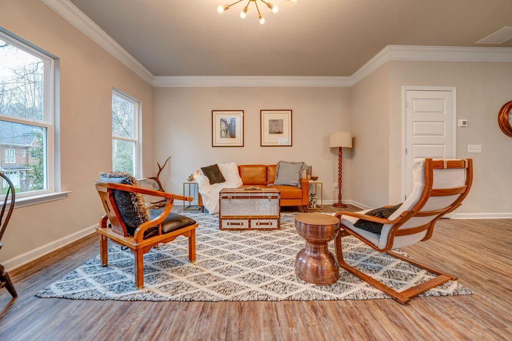 Staged living room with an orange sofa, wood-framed lounge chairs, and a patterned rug.