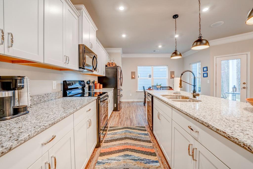 Kitchen with white cabinets, stainless steel appliances, and a large stone island with a sink.