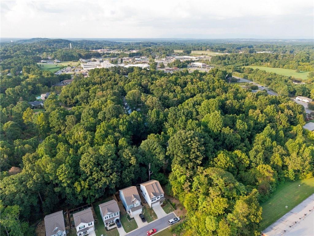 Aerial view of homes bordering dense woodland, with a residential street and distant commercial buildings.