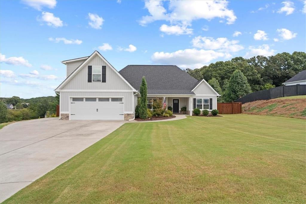 Light-colored house with a two-car garage, covered entry, broad lawn, and concrete driveway.