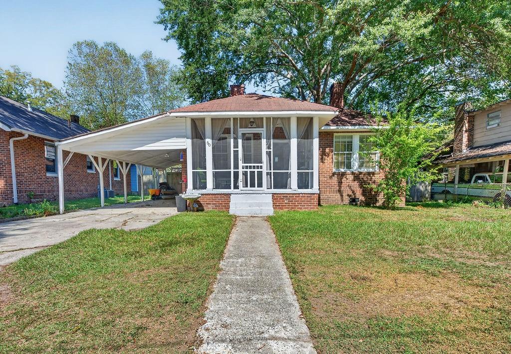 Brick house with a screened front porch and attached carport beneath mature trees.