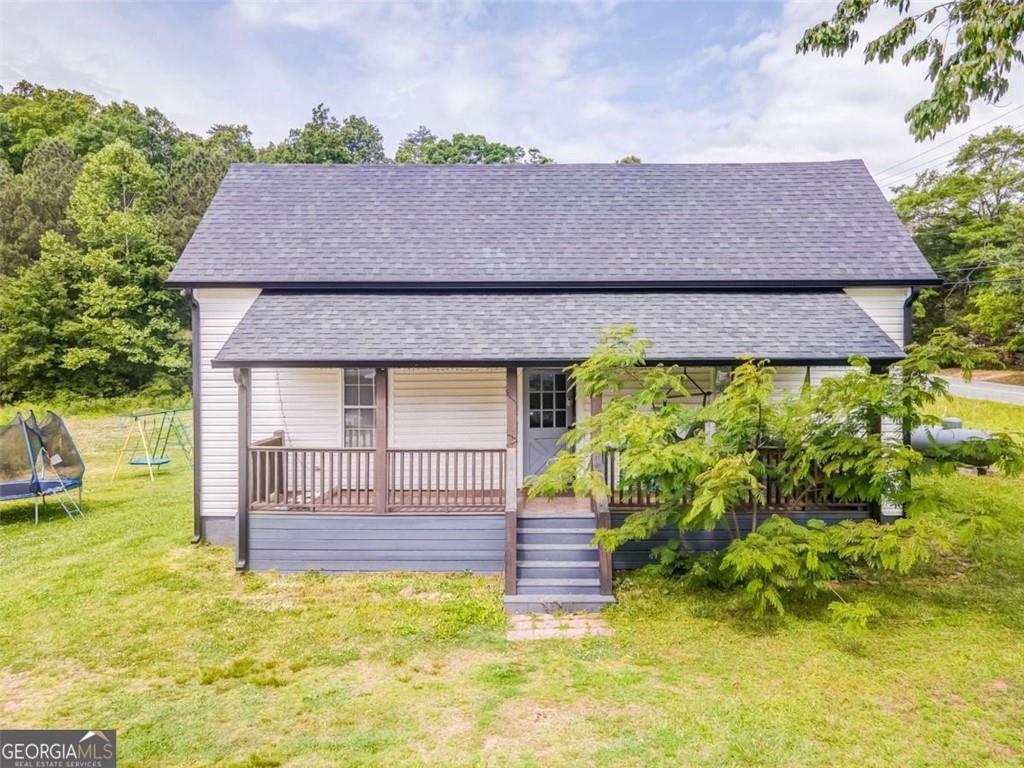 Small gray-and-white house with a covered porch, front steps, and a swing set on the lawn.