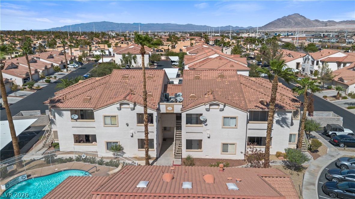 Apartment complex with a swimming pool, palm trees, and mountains in the background.