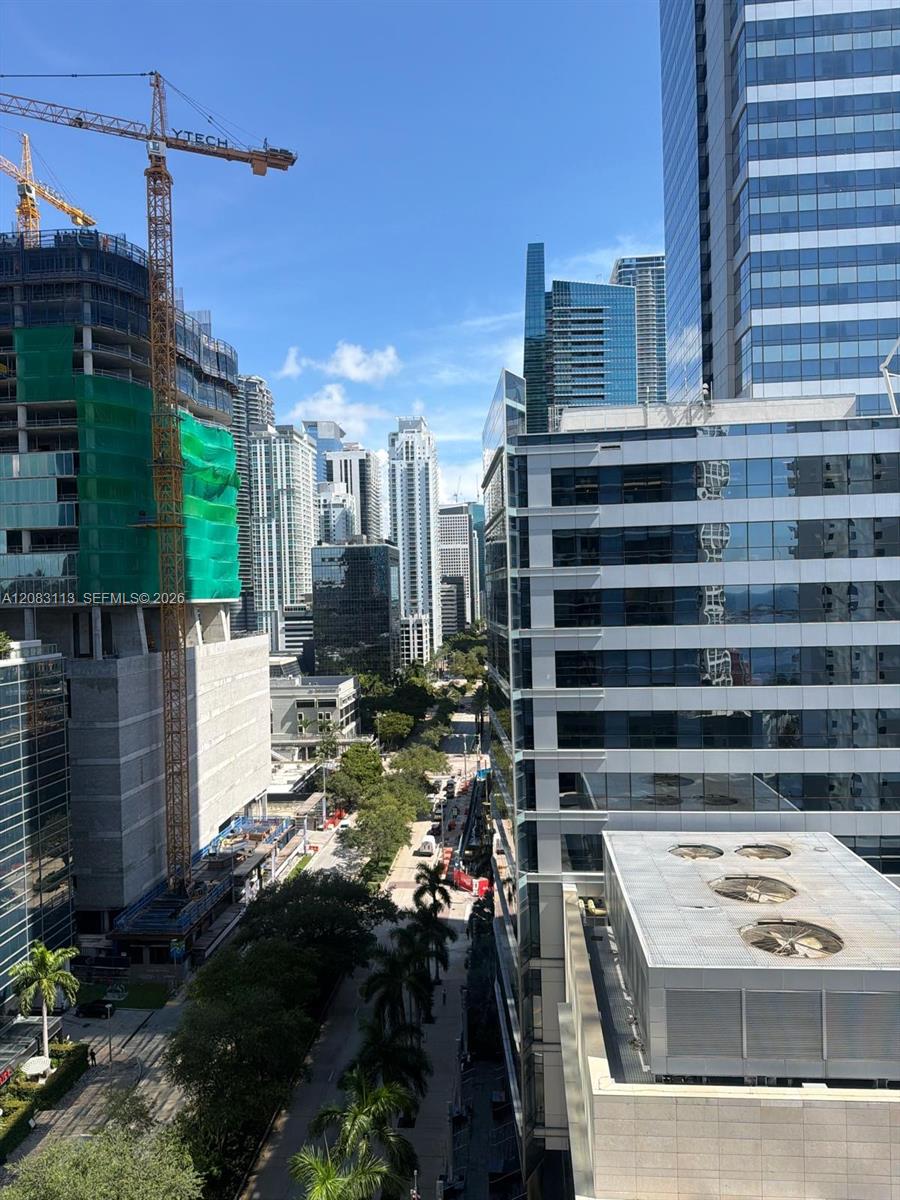Downtown Brickell skyline viewed between high-rises, with a construction crane and tree-lined street below.