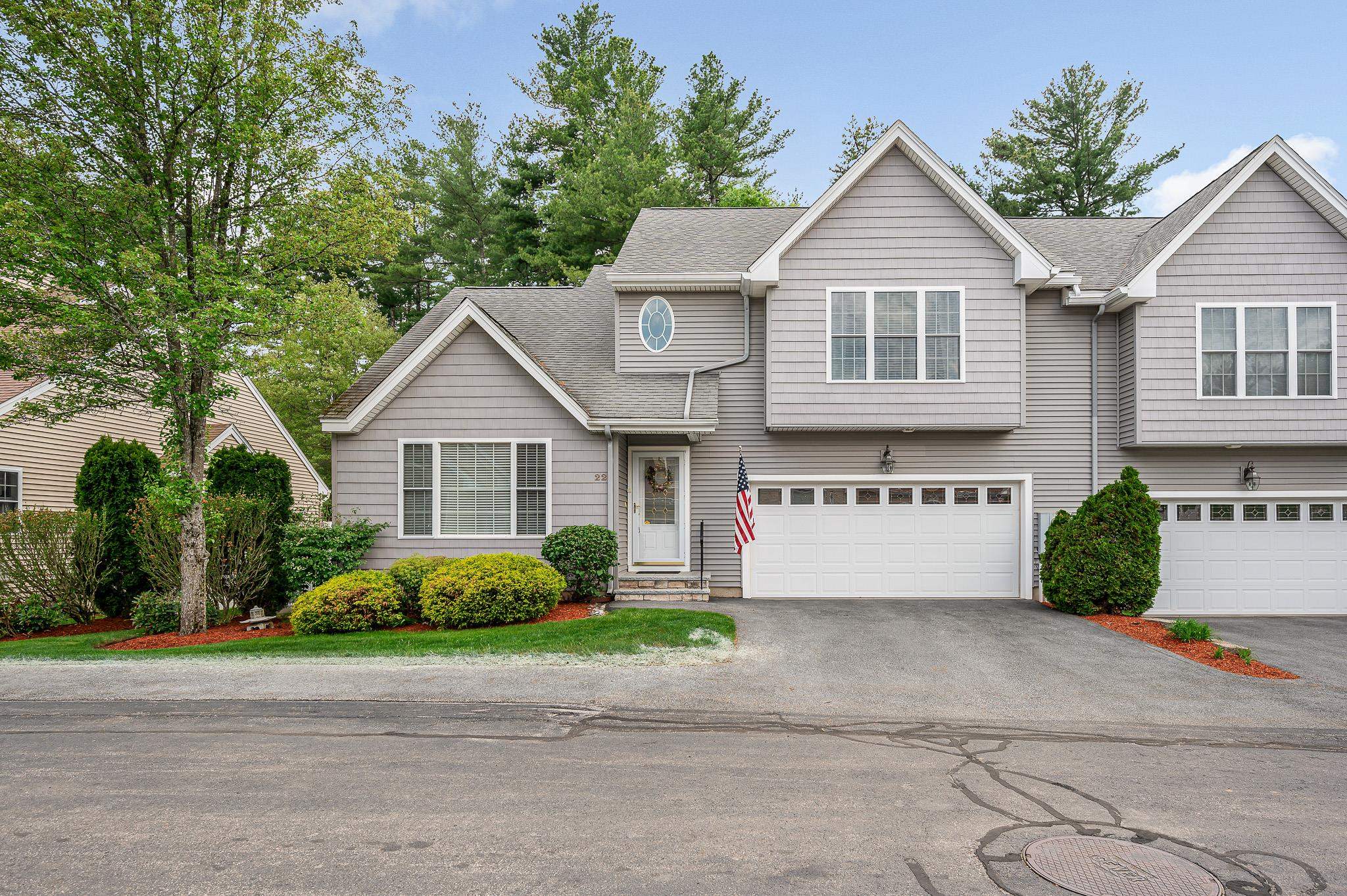 Gray two-story home with gabled roof, double garage, landscaped shrubs, and an American flag by the entrance.