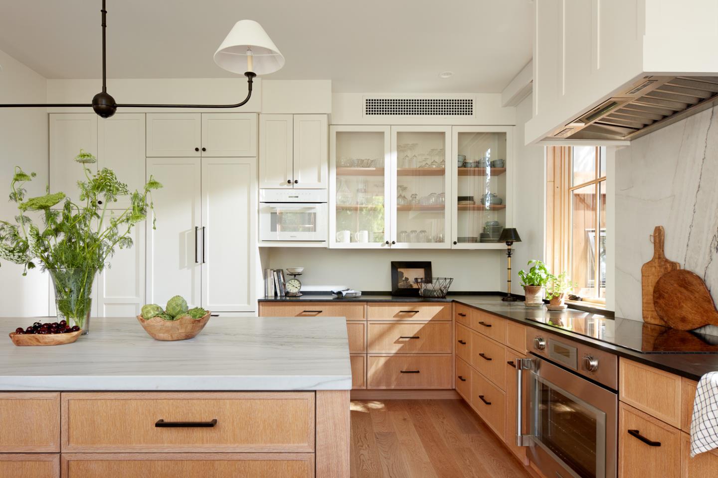 Bright kitchen with a large stone island, white cabinets, and warm wood cabinetry.