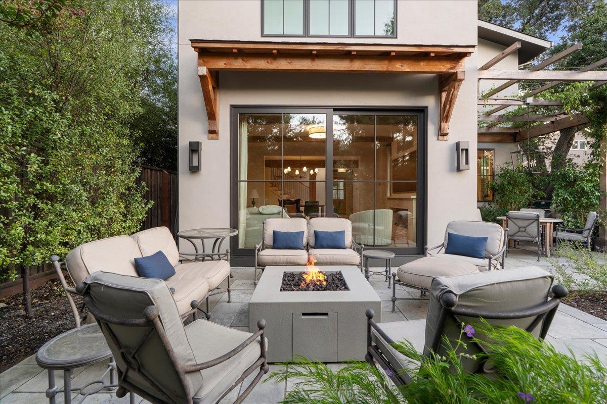 Furnished backyard patio with cushioned seating around a lit fire pit beside the home's glass doors.