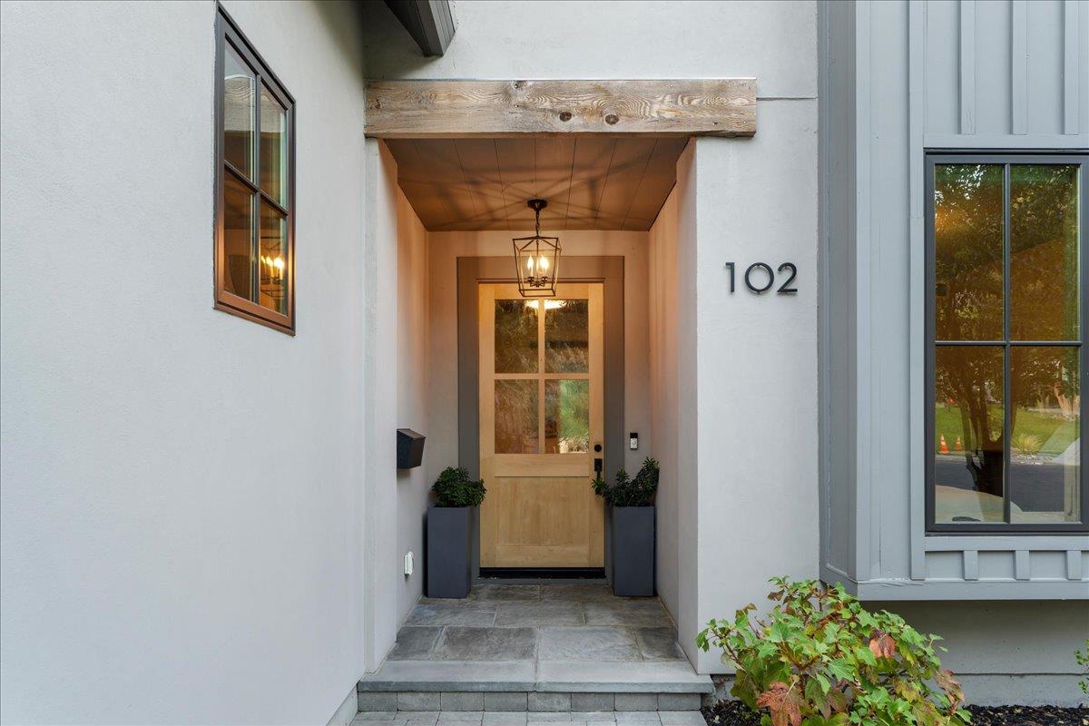 Home entrance with a light wood-and-glass door, stone steps, and planters beside the number 102.