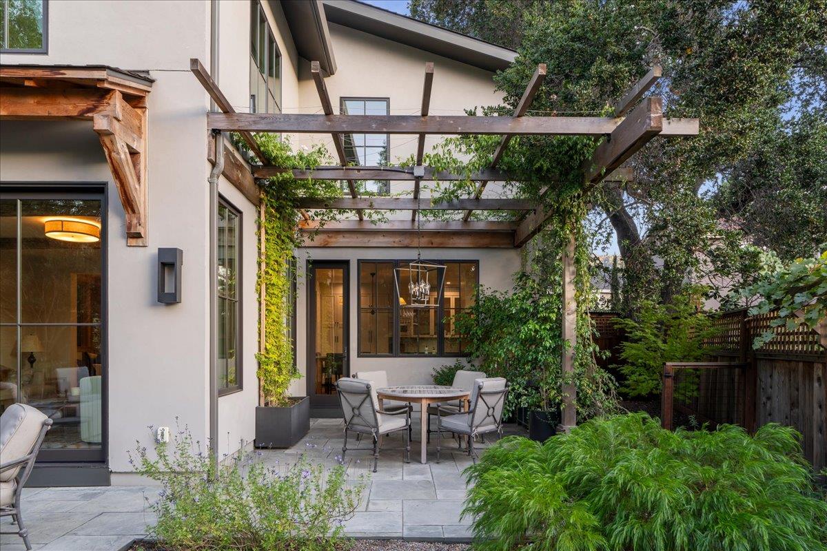 Stone patio with outdoor dining beneath a leafy timber pergola.