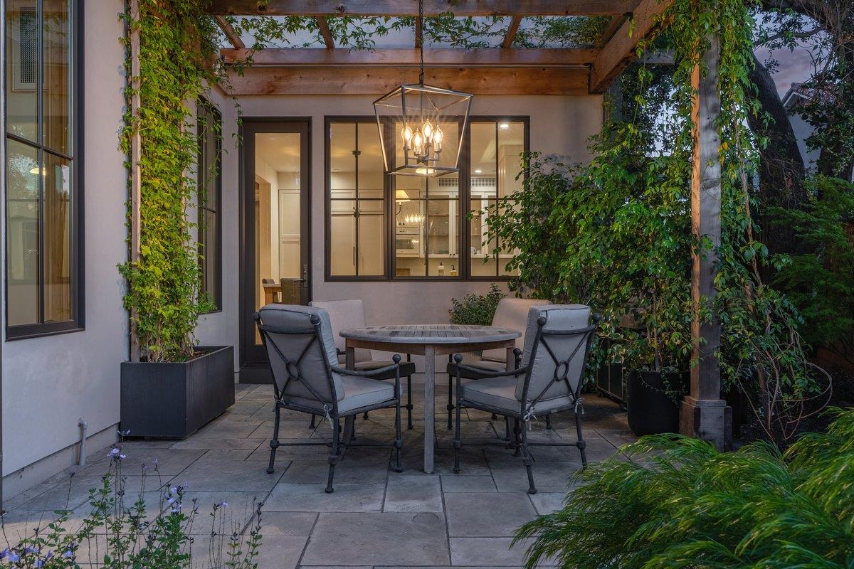 Stone patio with a timber pergola, round table, cushioned chairs and climbing greenery.