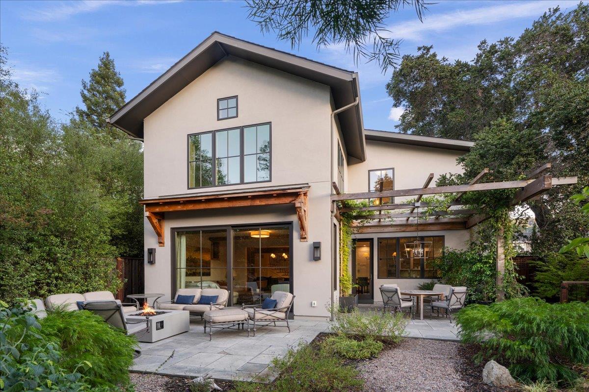 Home’s rear patio with outdoor seating, a fire table, and a timber pergola.