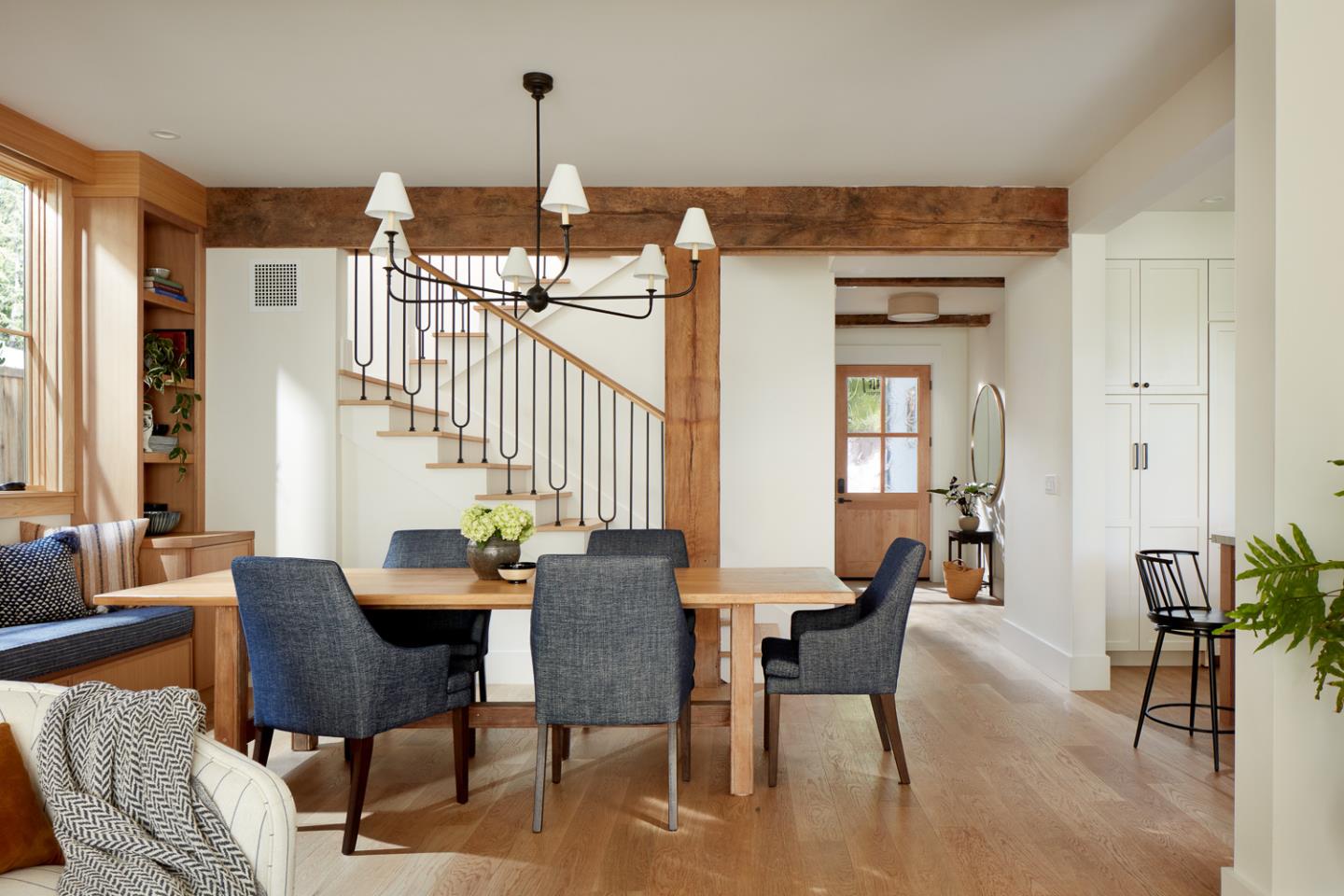 Dining area with a wooden table, built-in window seat, and staircase beneath exposed timber beams.