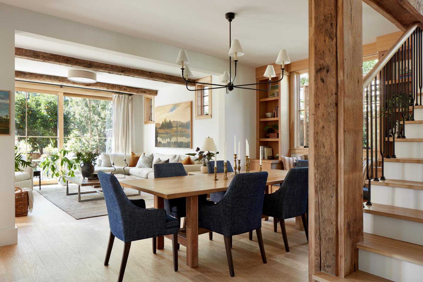 Open-plan dining and living room with a timber dining table, exposed beams, and staircase.