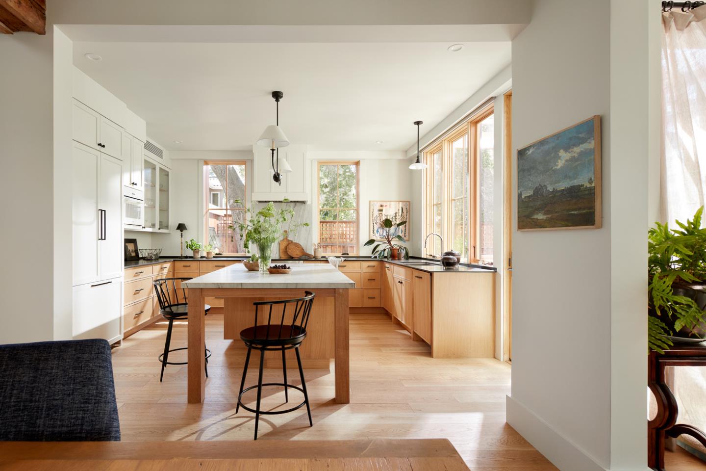 Bright kitchen with a large stone-topped island, warm wood cabinets, and tall windows.