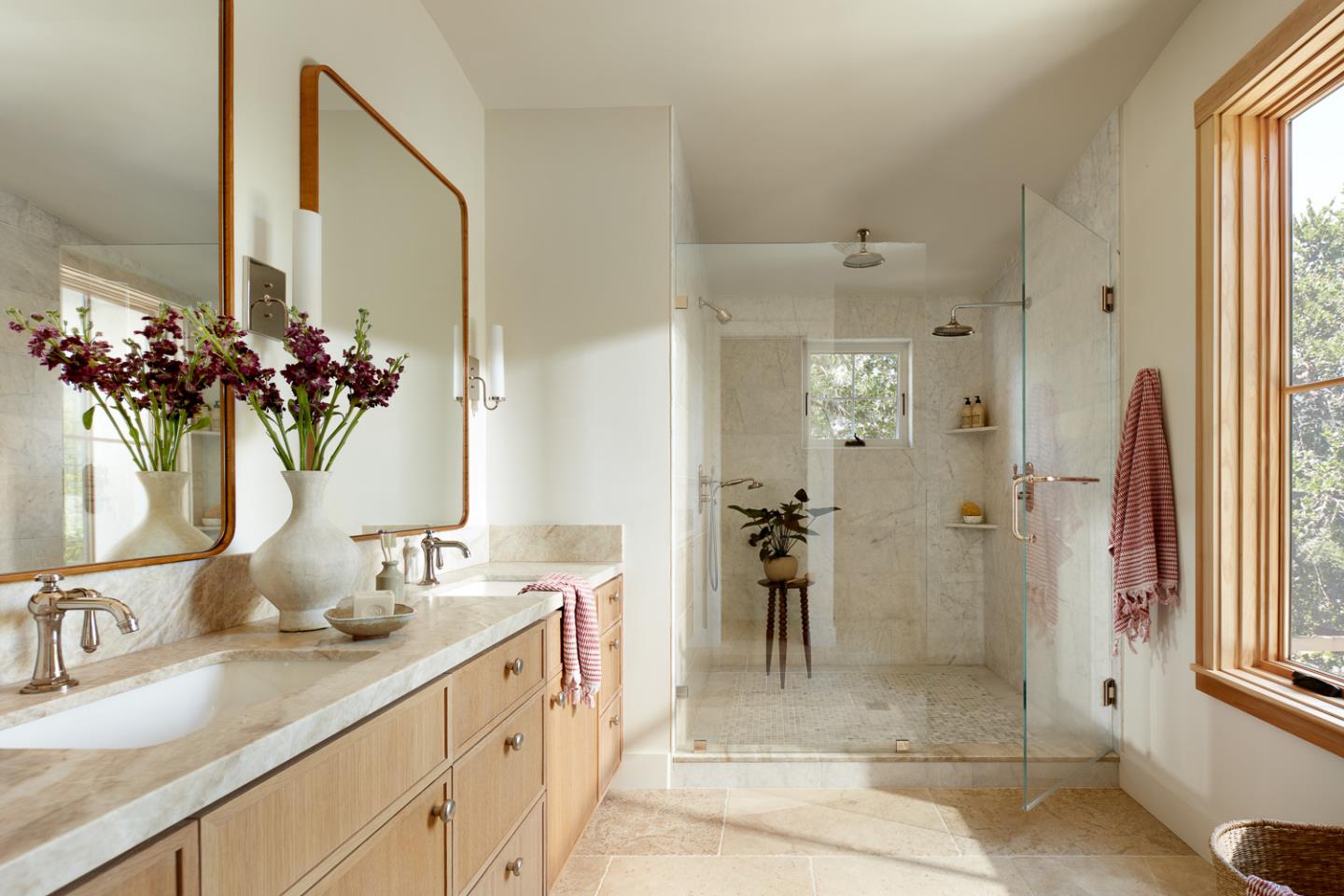 Bright bathroom with a long wood vanity and spacious glass-enclosed marble shower.