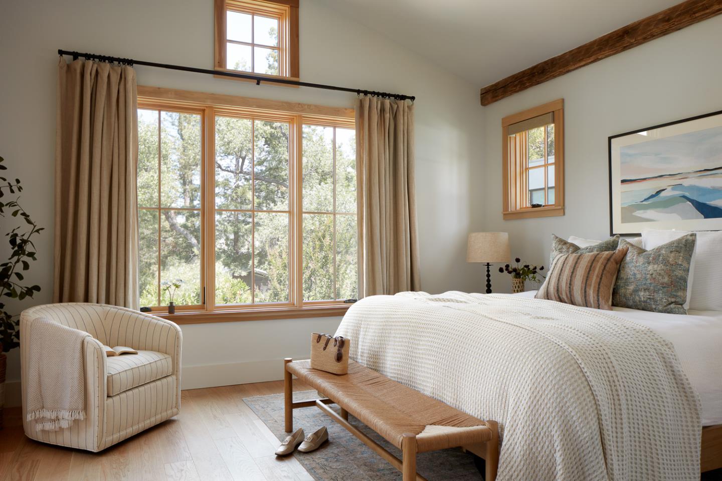 Staged bedroom with a white-covered bed, tall wood-trimmed windows, and an upholstered armchair.