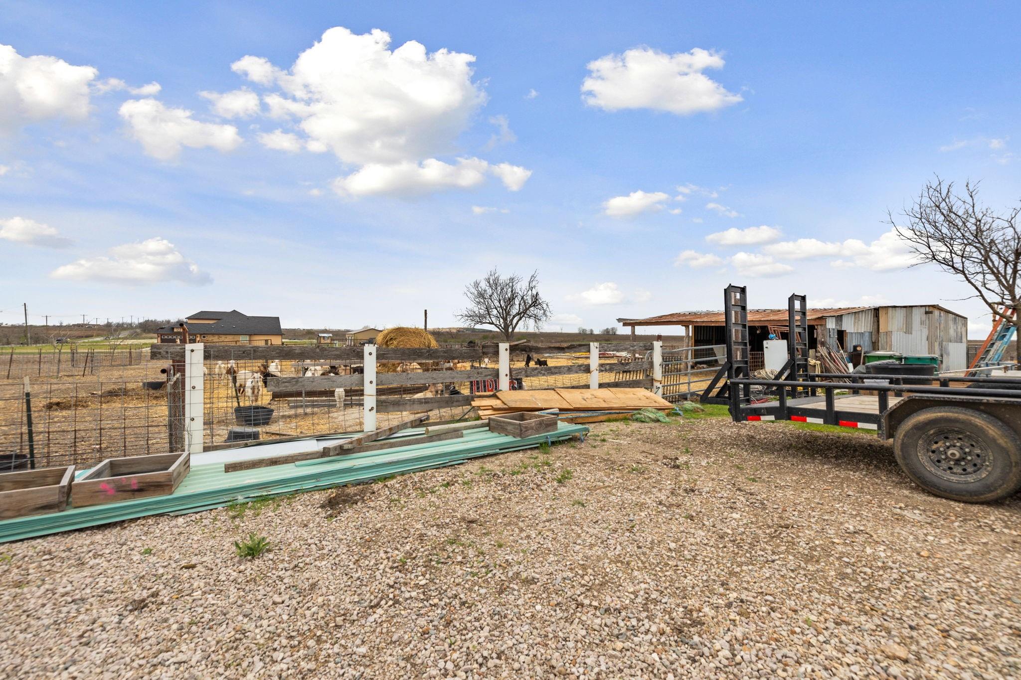Rural property with fenced livestock pens, a metal shed, and a utility trailer in a gravel yard.