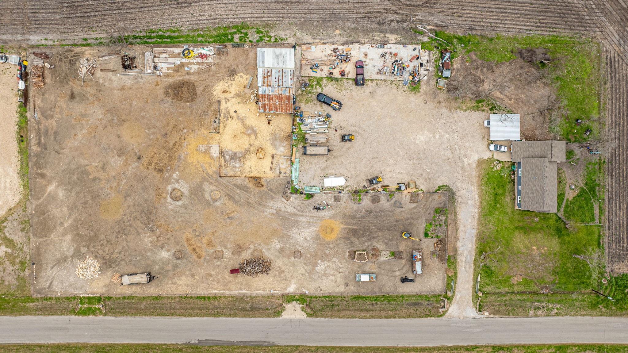 Aerial view of a large construction site beside an existing house and paved road.