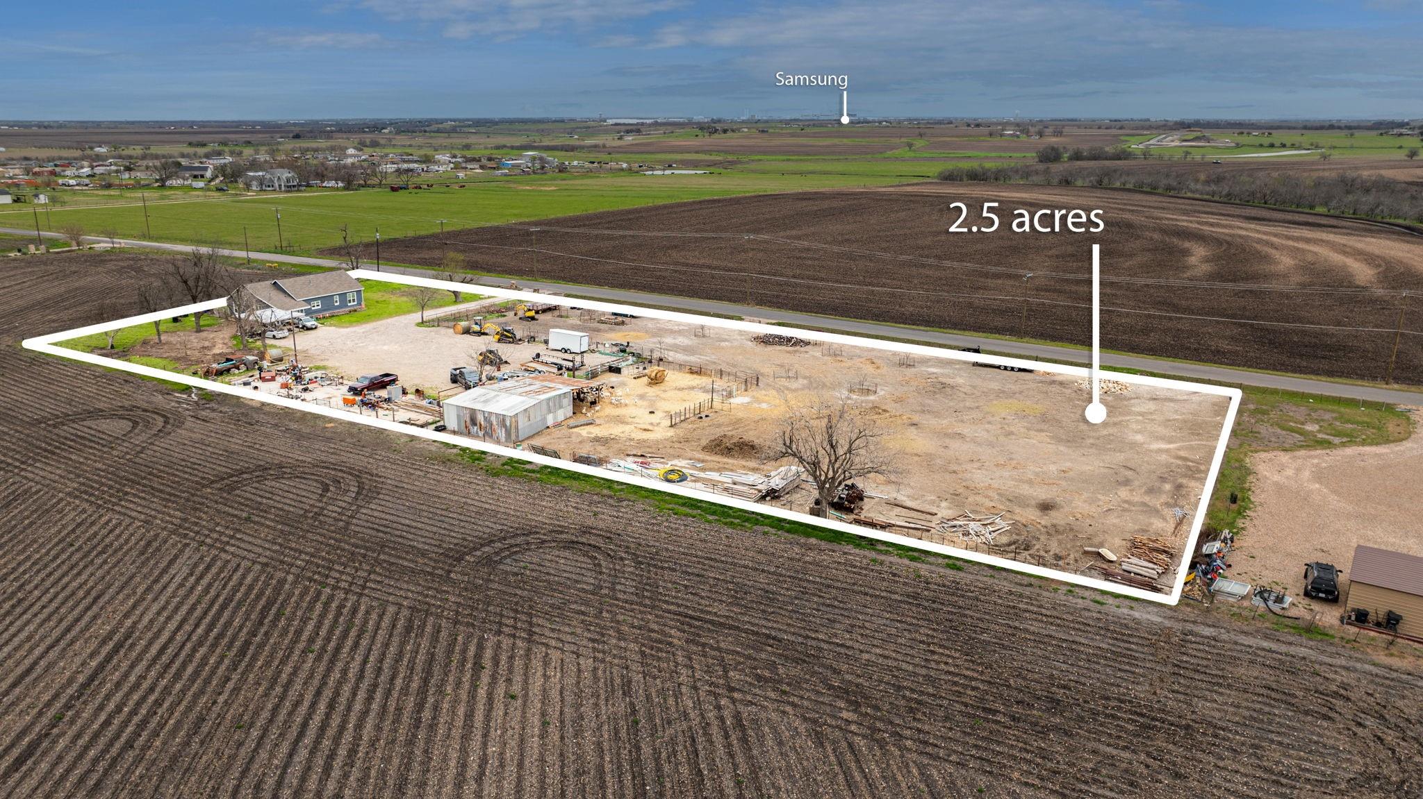 Aerial view of a 2.5-acre rural property outlined beside a road, with a house, sheds, and equipment.