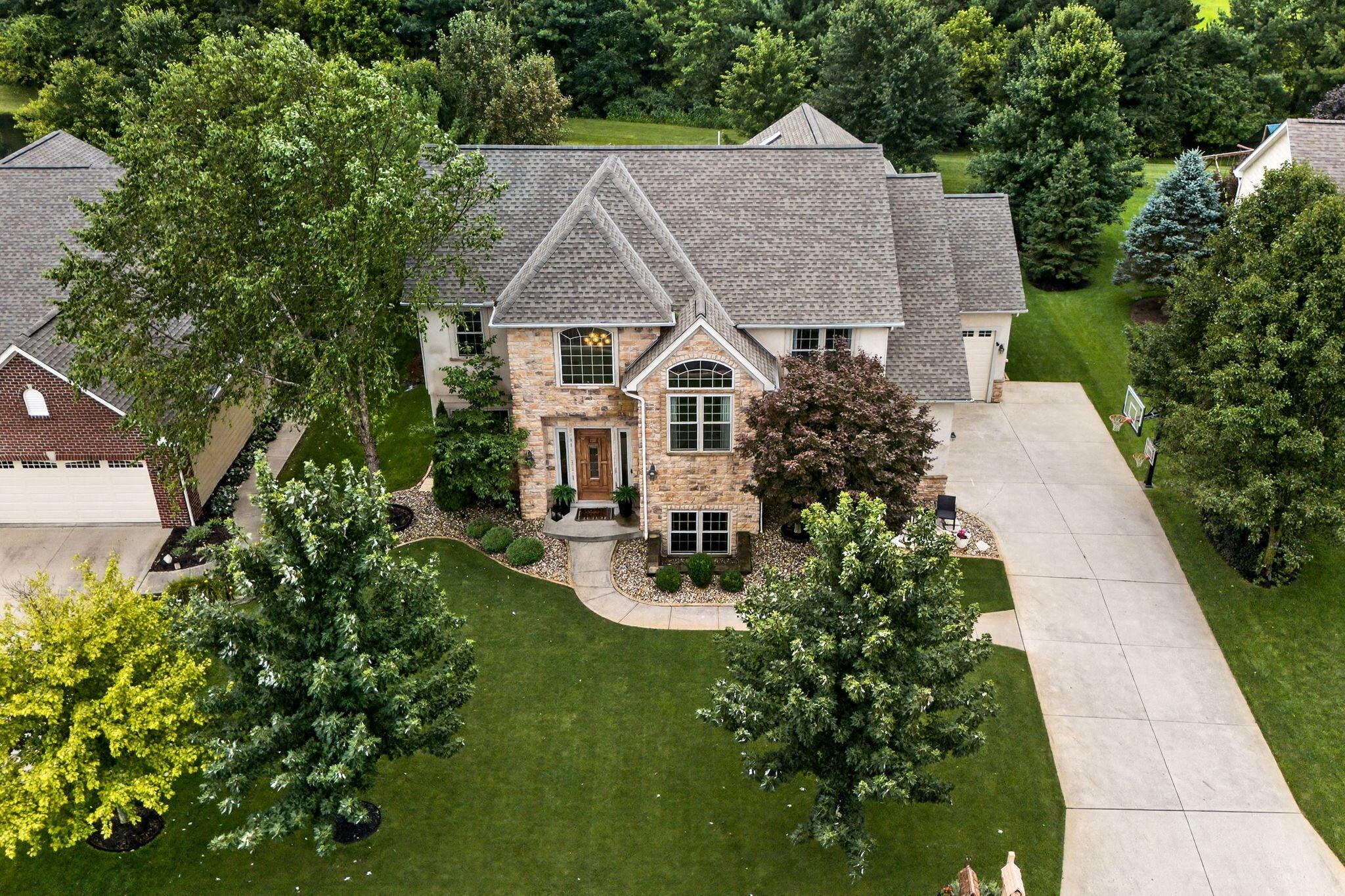Stone-front home with landscaped grounds and a broad driveway, seen from above.