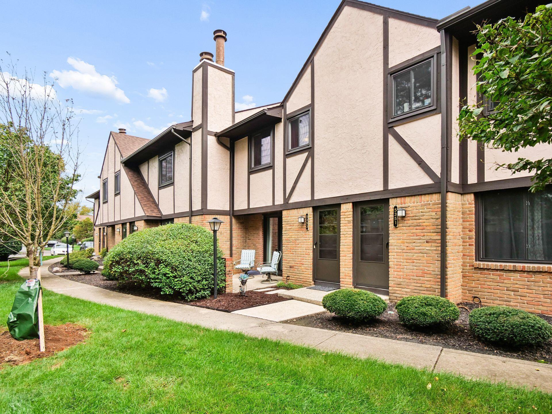 Attached home exterior with cream stucco, brick lower walls, landscaped shrubs, and a small patio.