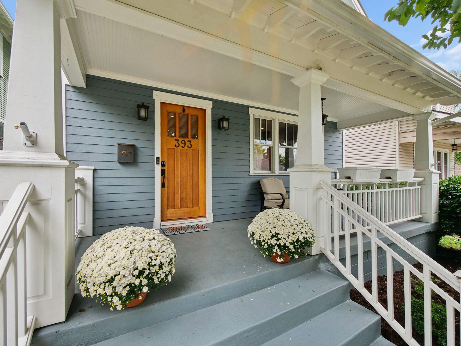 Home entrance with a covered porch, wooden door marked 393, white railings, and flower planters.