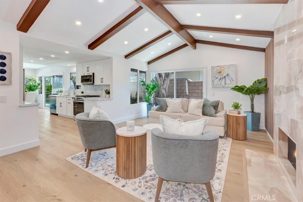 Living room with exposed wood ceiling beams, fireplace, and an open kitchen.
