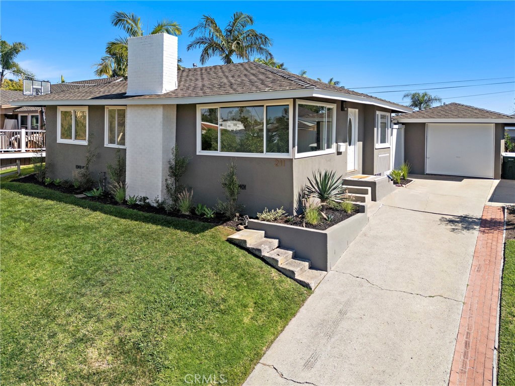 Single-story gray stucco home with a broad driveway, attached garage, and front lawn.