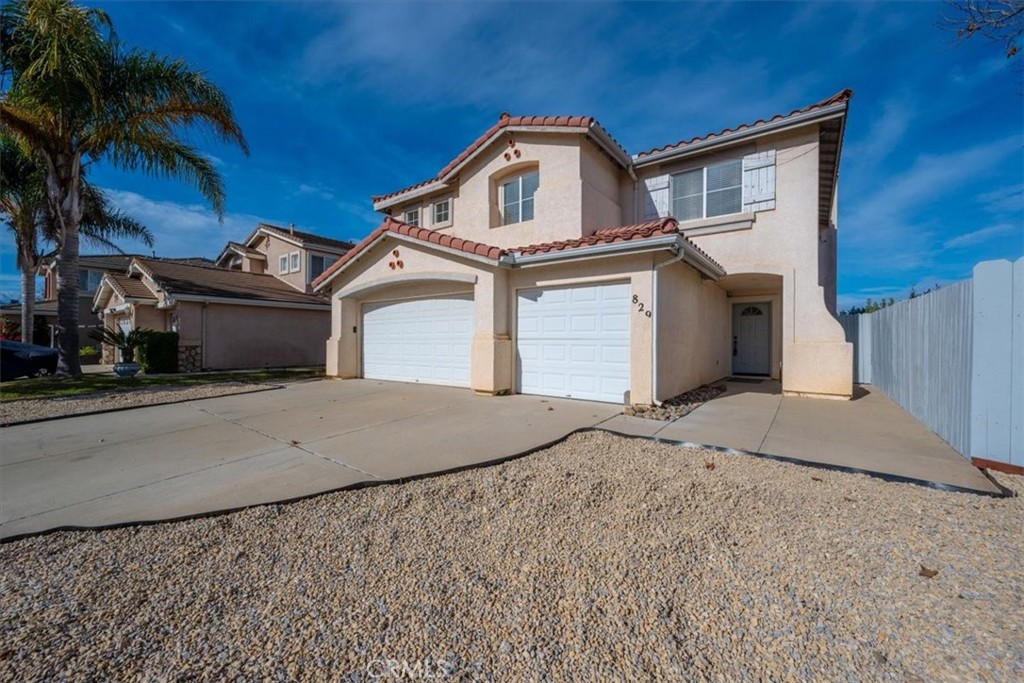 Two-story stucco house with red tile roofs, double garage doors, gravel landscaping, and a palm tree.