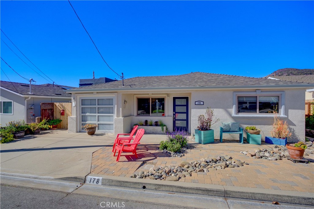 Single-story stucco home with a blue front door, garage, and red patio chairs.
