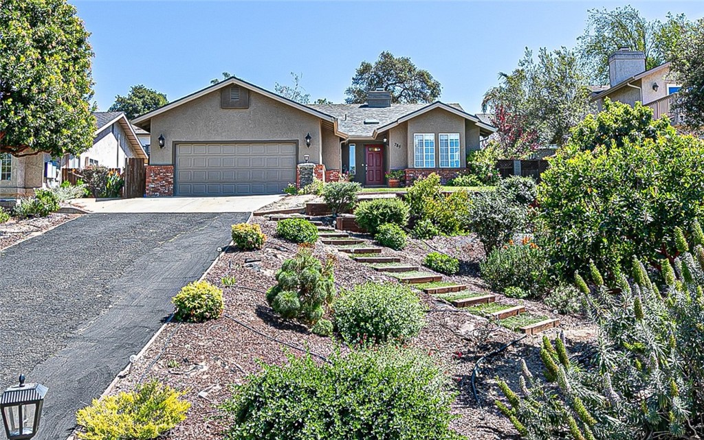 Single-story stucco home with a gray garage, red front door, and landscaped stepped walkway.