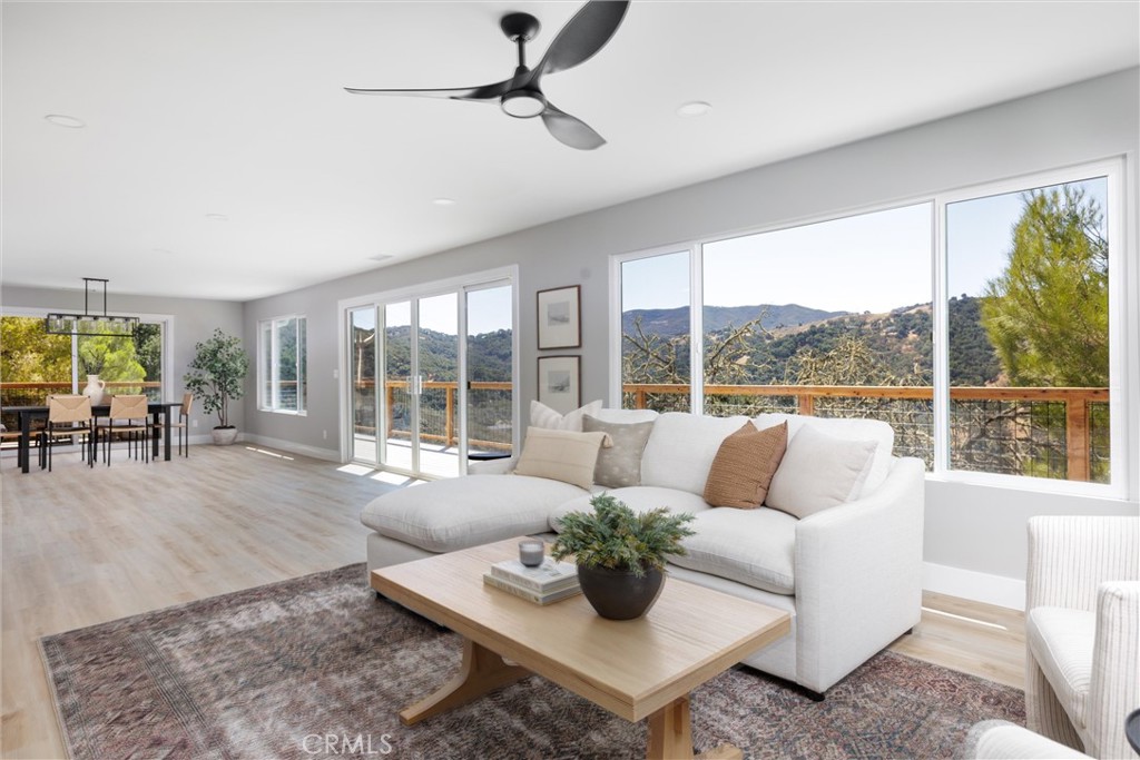 Staged living room with a white sectional and broad windows overlooking wooded hills.