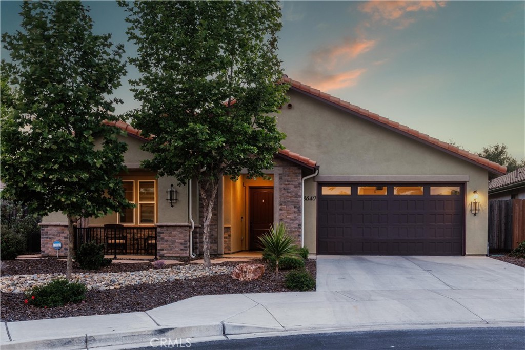 Single-story stucco home with stone accents, covered entry, and two-car garage at dusk.