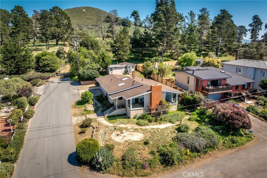 Aerial view of a single-story home on a corner lot beside wooded hills.