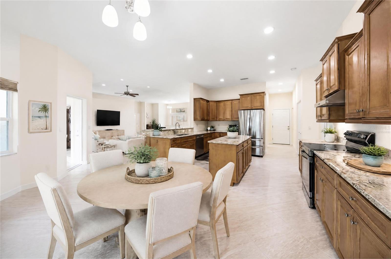 Open kitchen and dining area with wood cabinetry, granite counters, stainless appliances, and a round table.