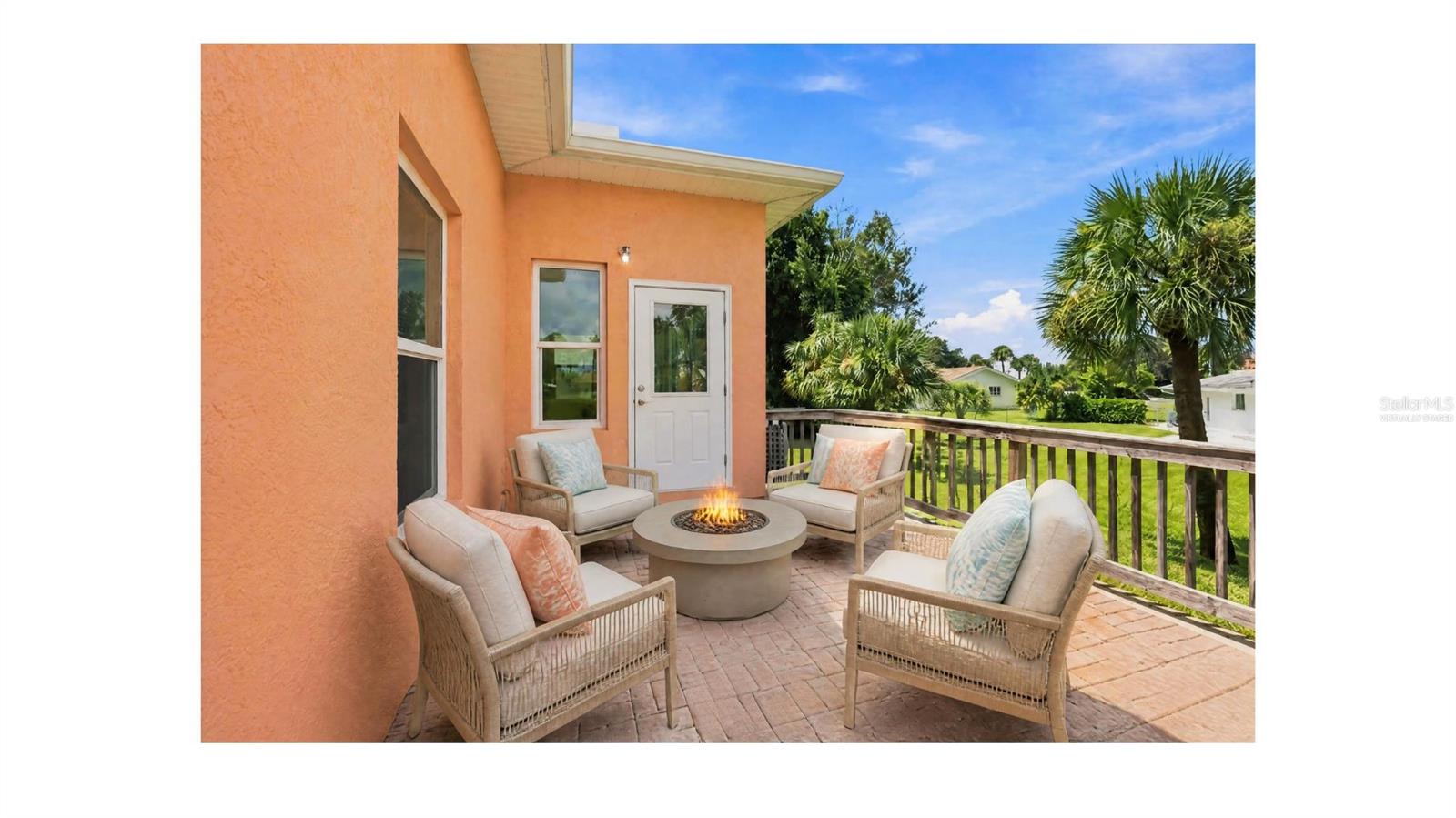 Furnished patio with wicker chairs around a fire pit beside a peach-colored home.