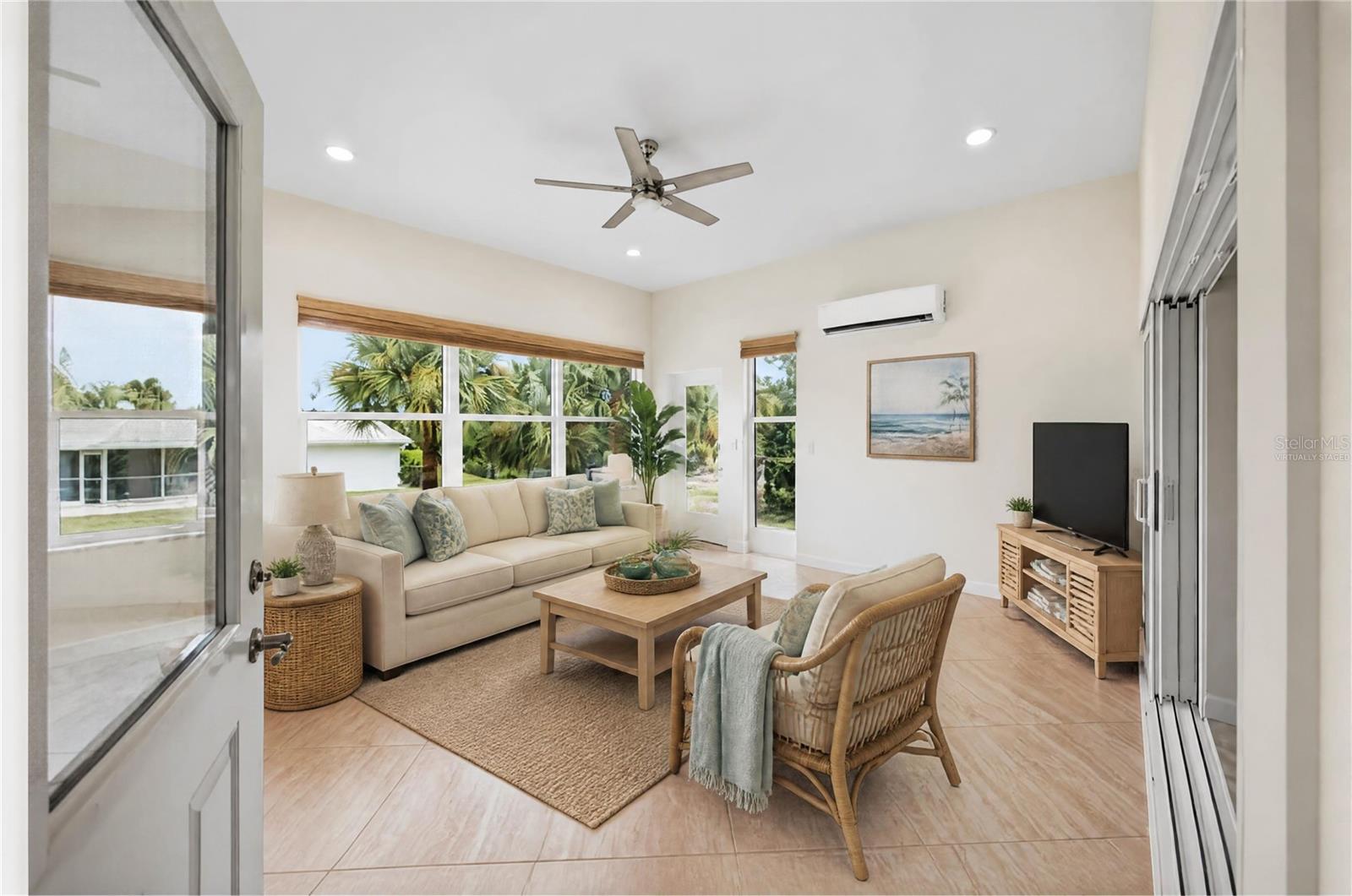 Bright living room with cream sofa, rattan chair, tiled floors, and large windows overlooking palms.