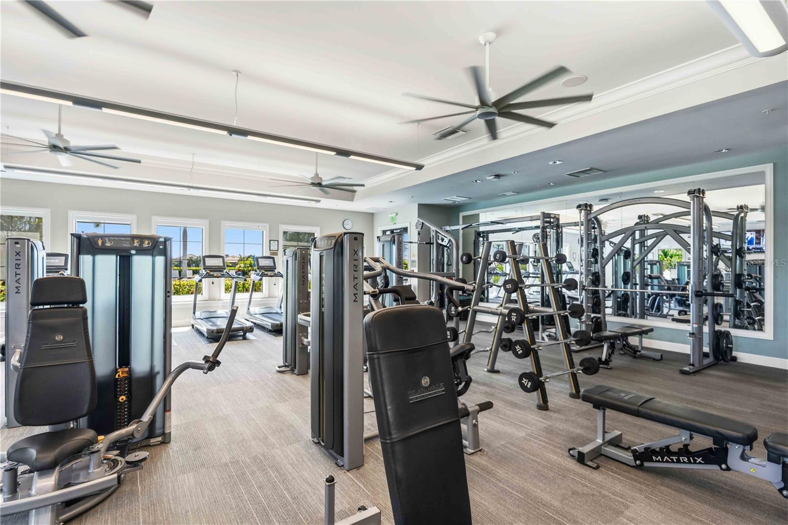 Fitness center with weight machines and treadmills beside large mirrored walls.