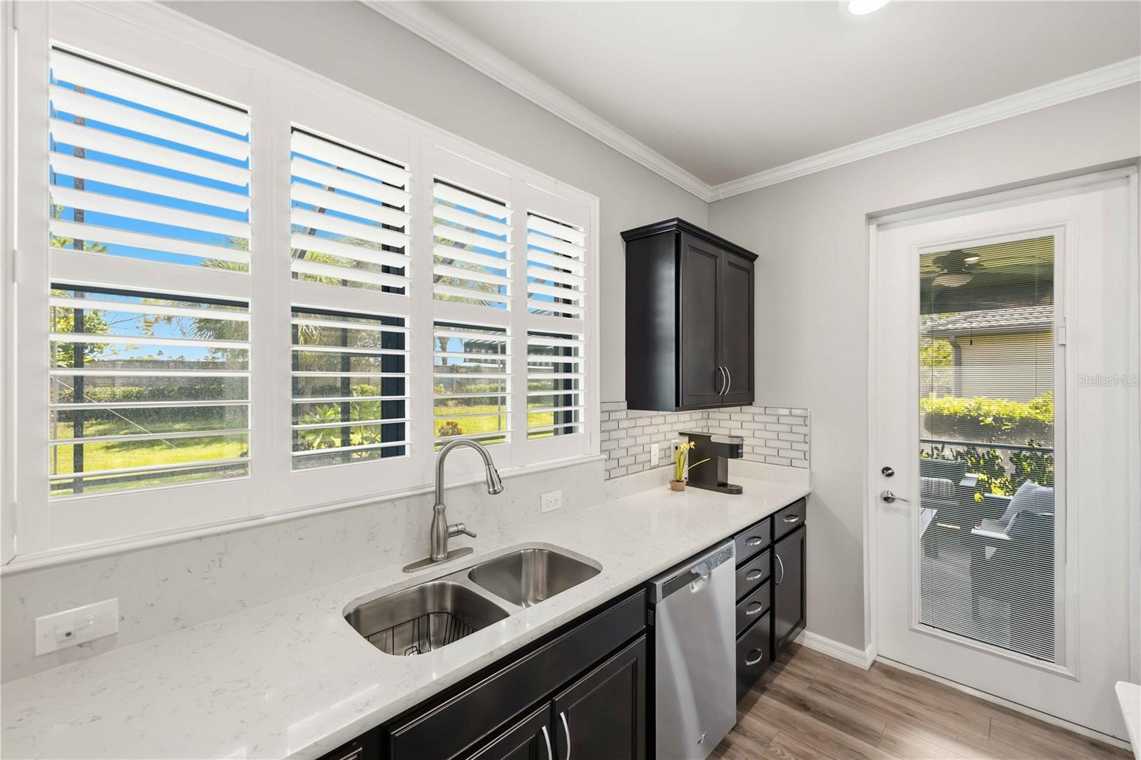 Kitchen with dark cabinets, white quartz counters, plantation shutters, and a glass-panel exterior door.