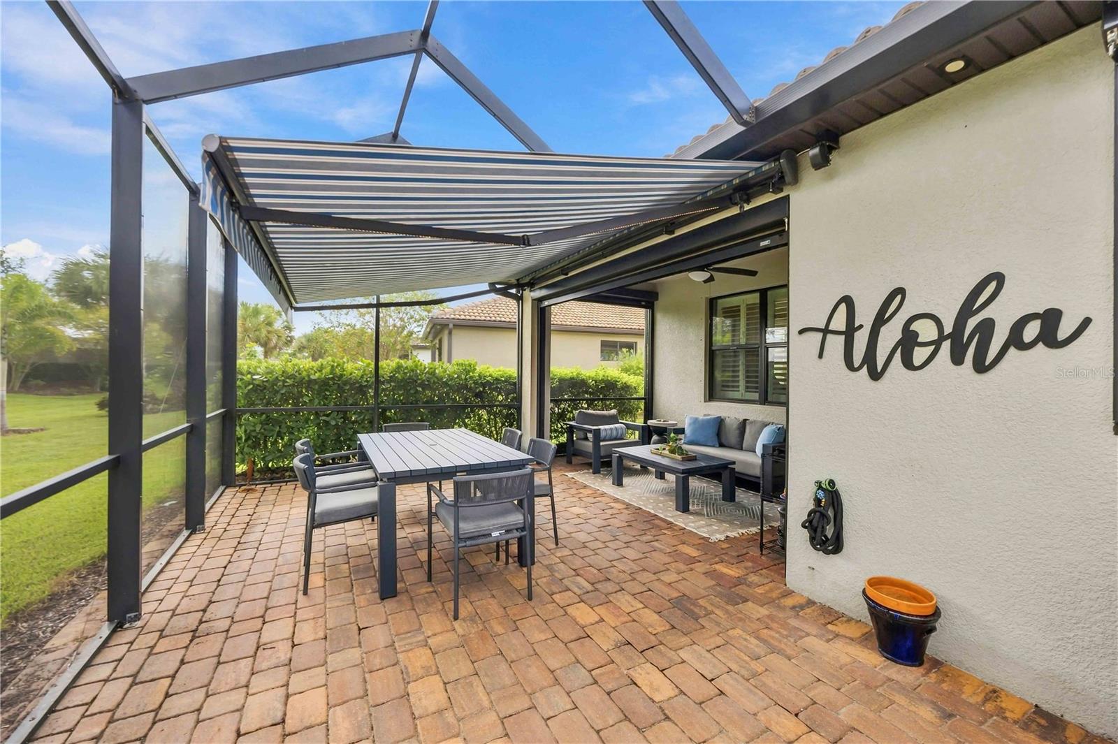 Furnished brick patio with dining and lounge seating beneath a striped retractable awning.