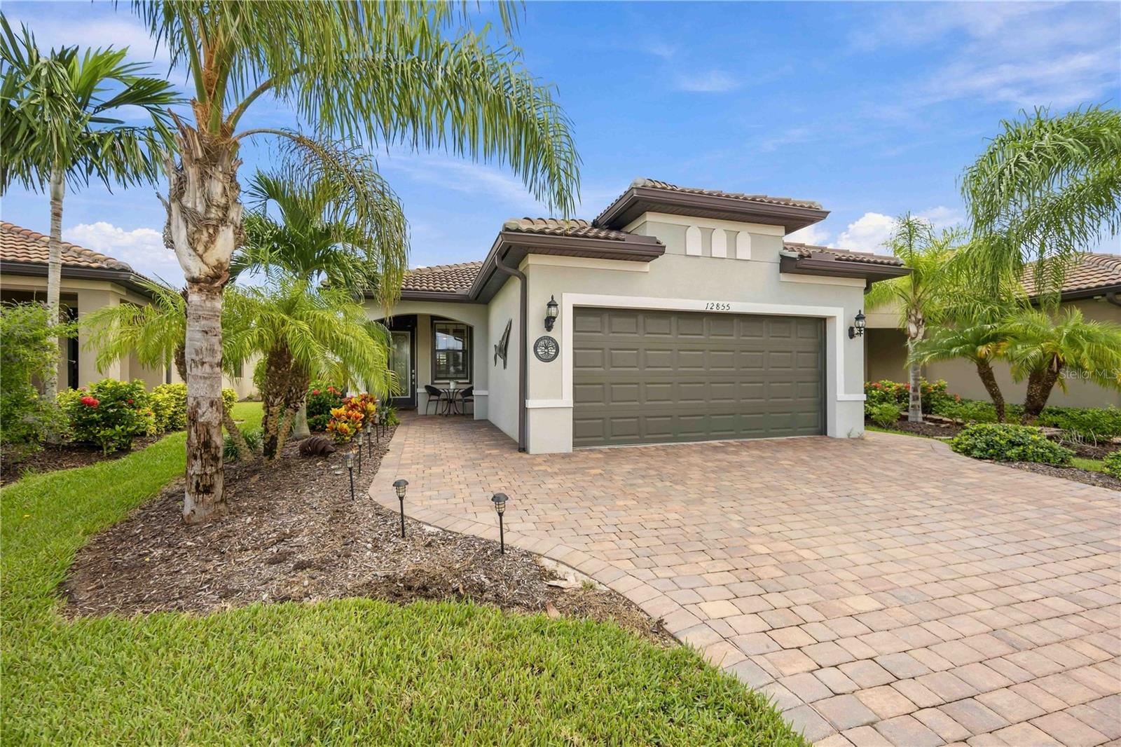 Home exterior with a wide garage, curved paver driveway, and tropical palm landscaping.