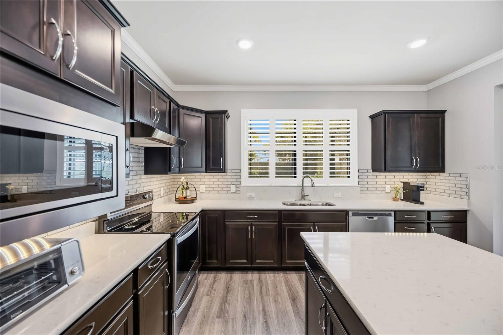 Kitchen with dark cabinets, white countertops, a large island, stainless steel appliances, and plantation shutters.
