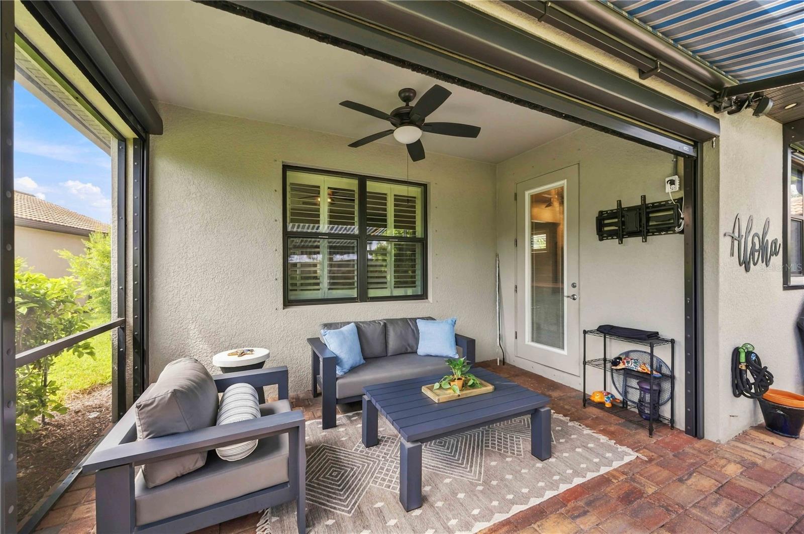 Screened patio with gray seating, a blue coffee table, brick pavers, and an overhead retractable awning.