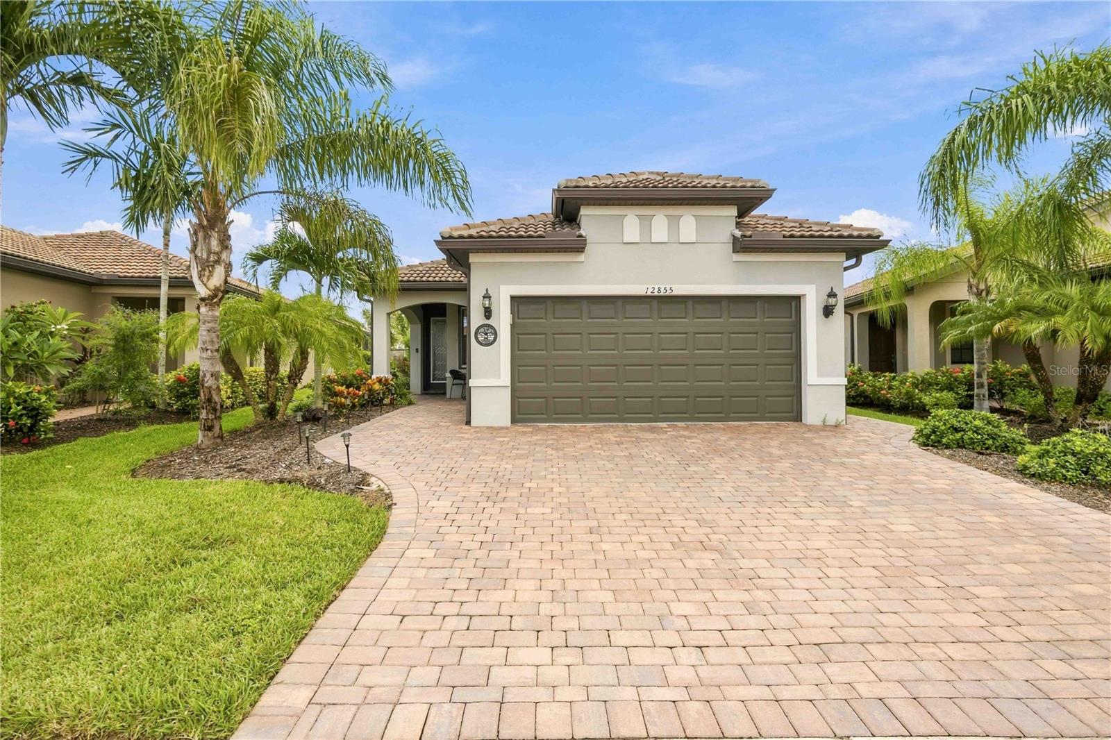 Home with a double garage, broad paver driveway, and palm trees in the front yard.