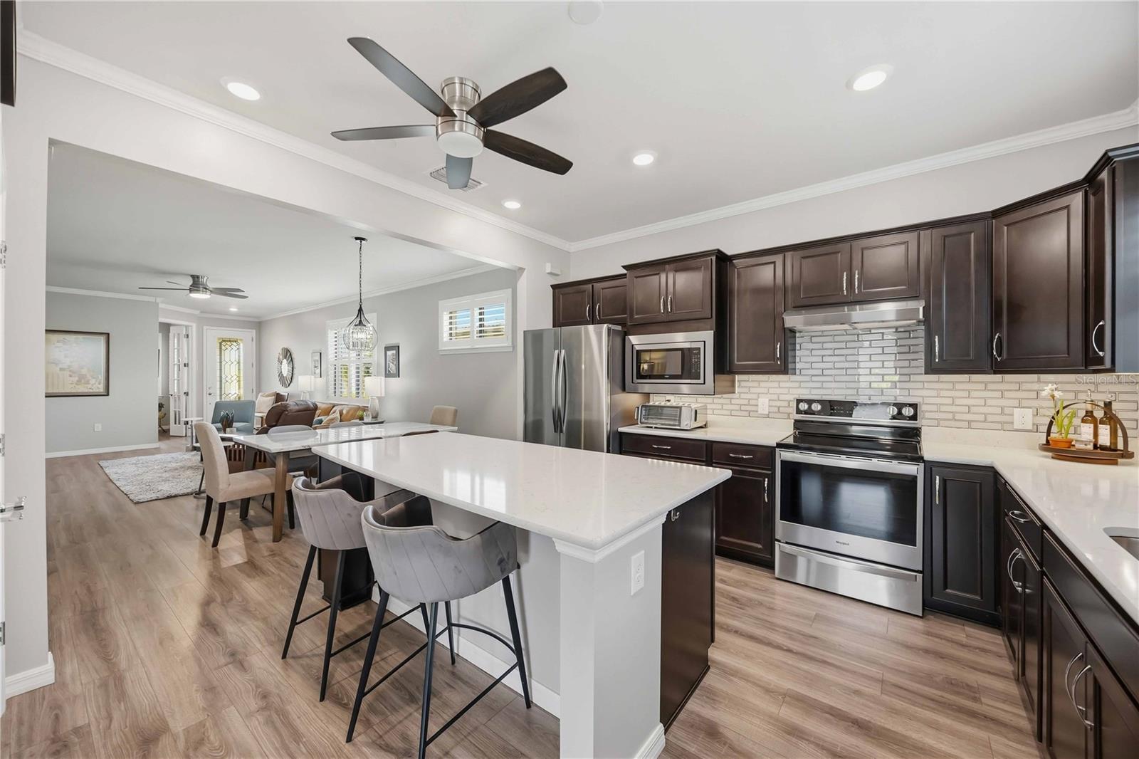 Open-plan kitchen with dark cabinets, stainless appliances, and a large white island beside the dining area.