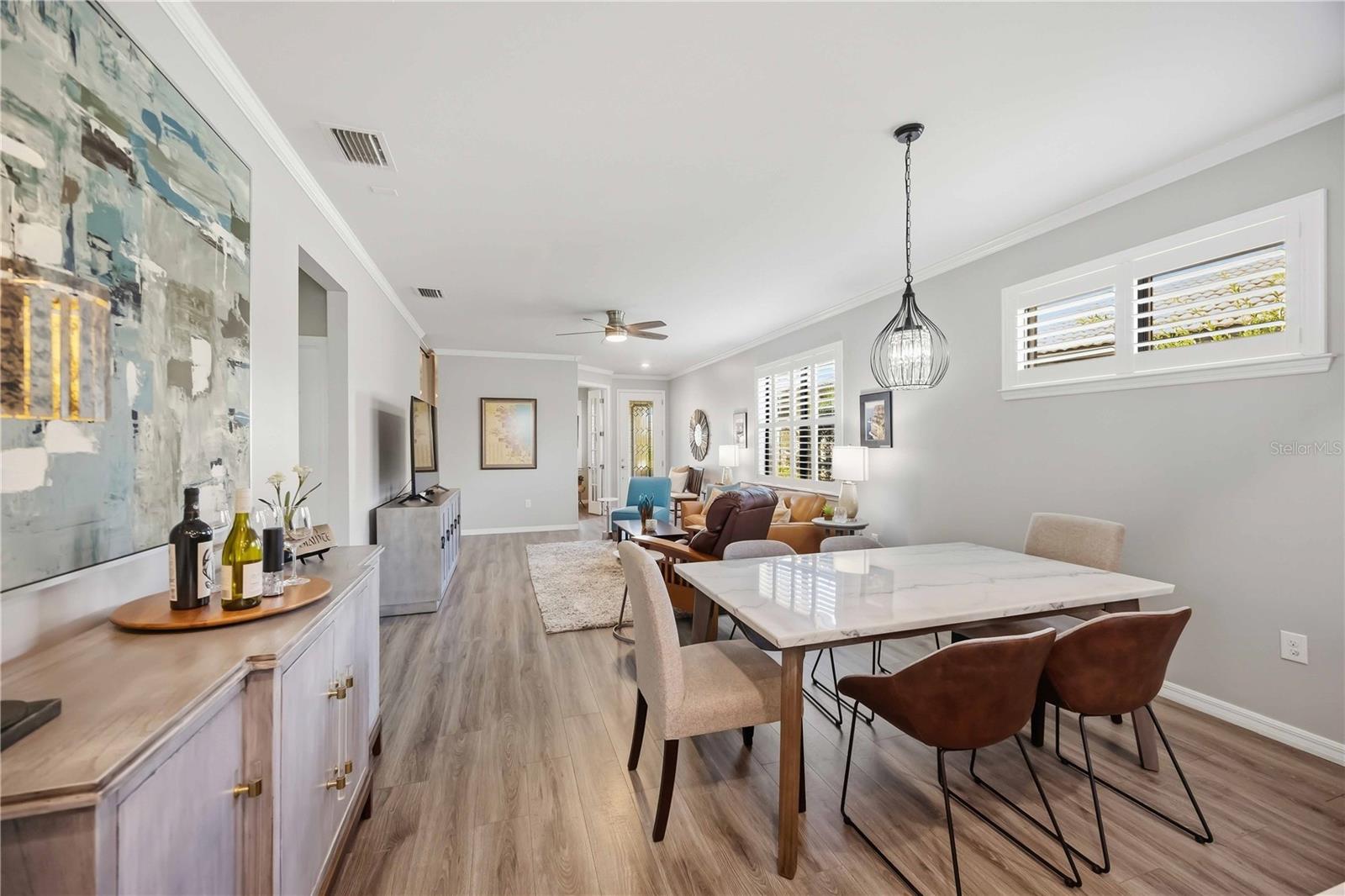 Open dining and living room with a marble-top table, upholstered chairs, and shuttered windows.