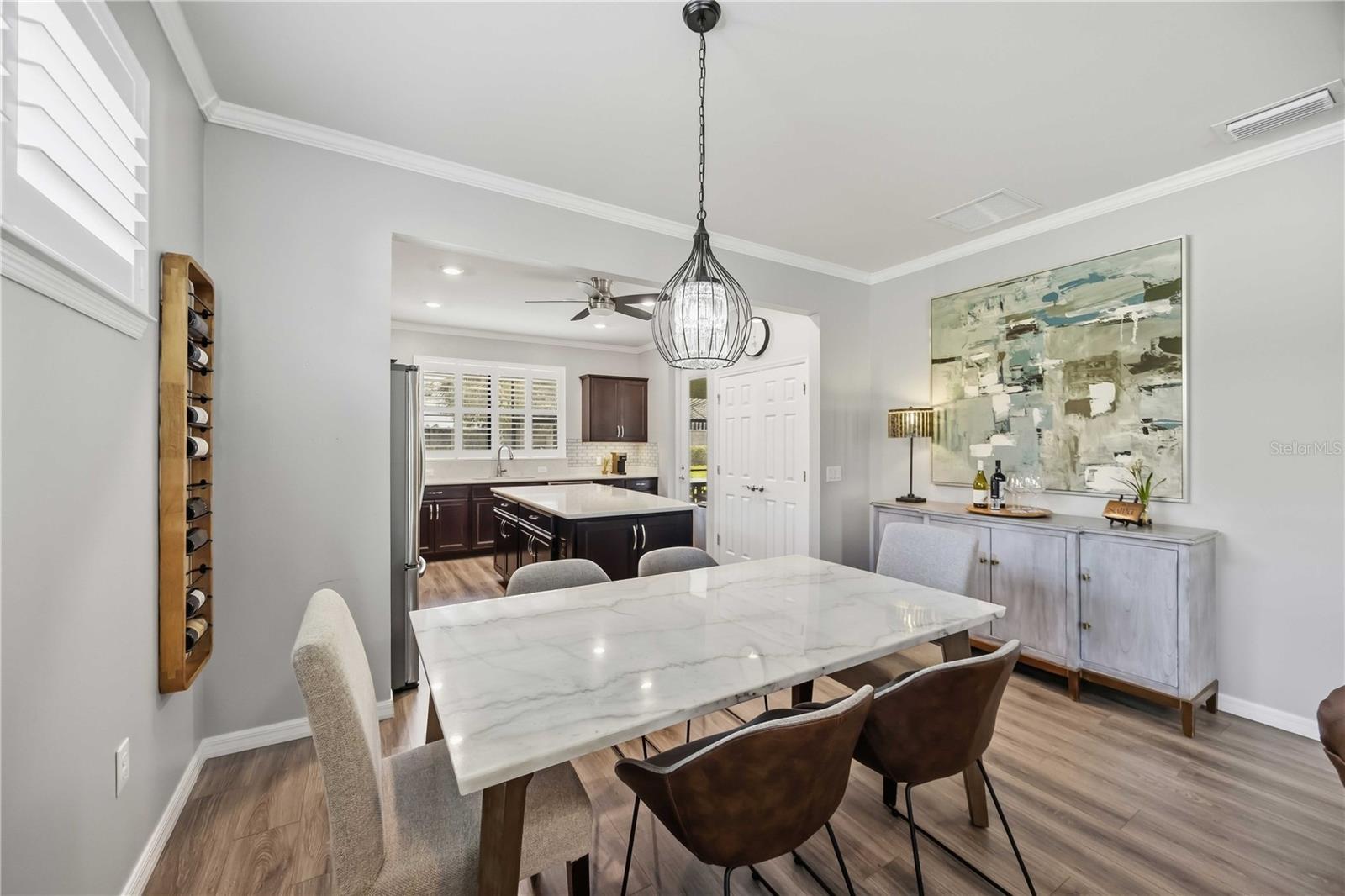 Dining room with a marble-look table and chandelier opening to a kitchen with dark cabinets.