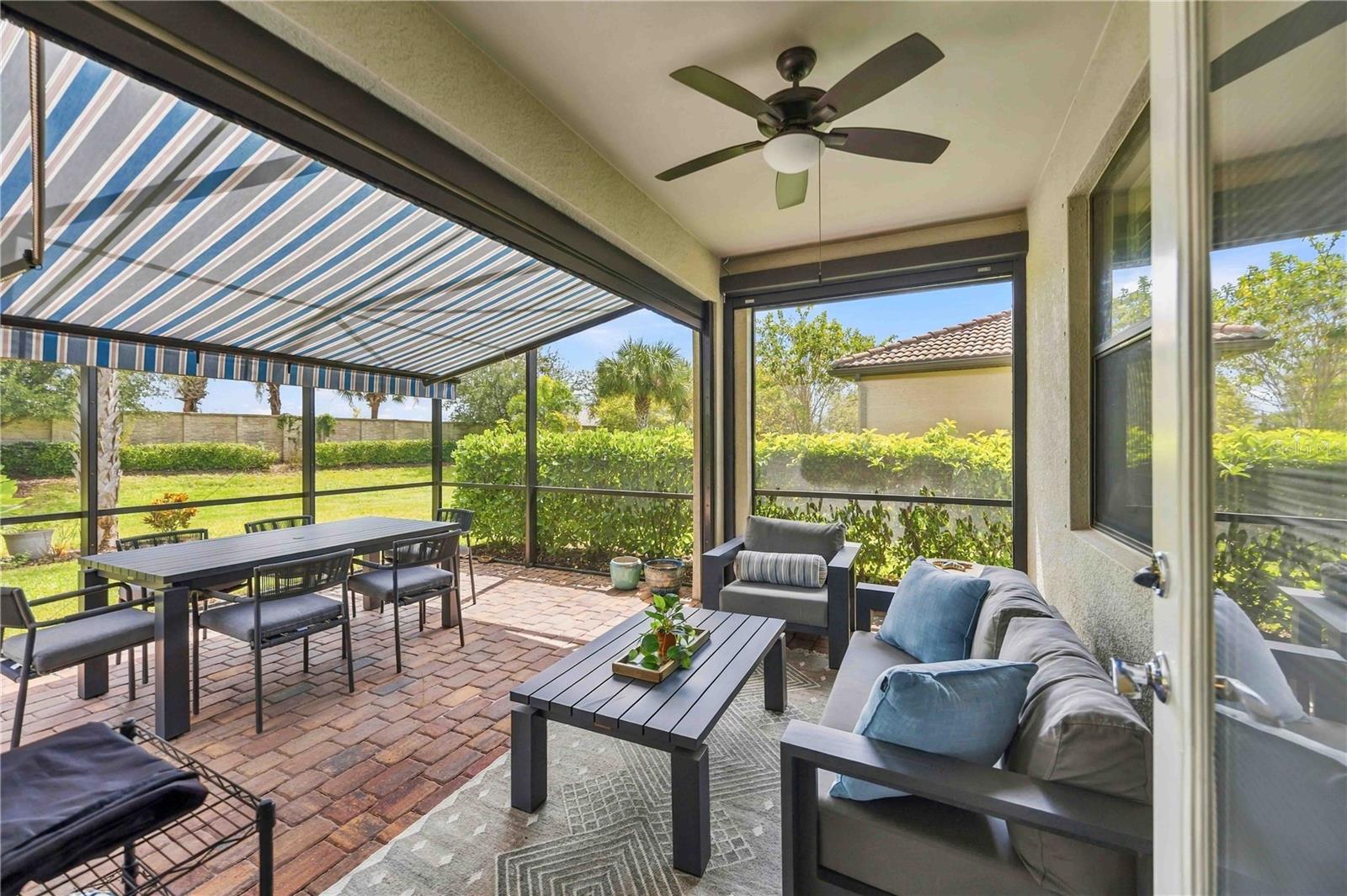 Covered patio with brick pavers, a striped awning, and dining and lounge furniture.