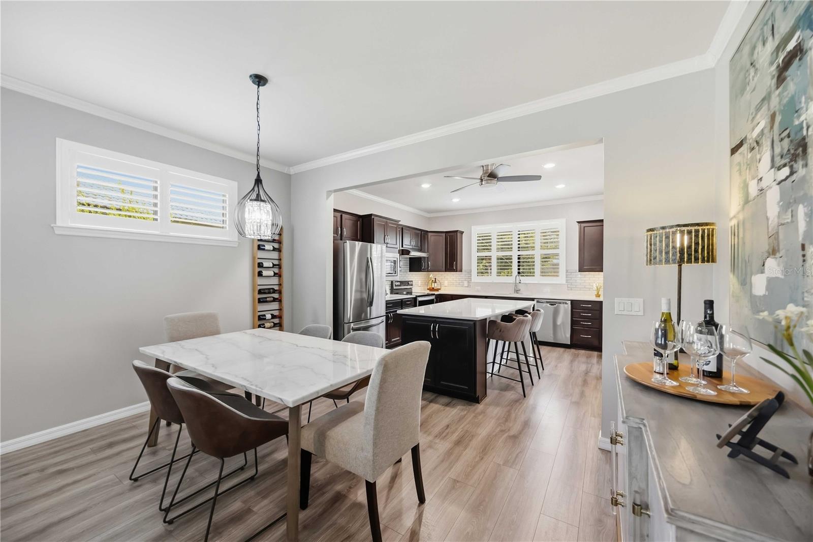 Dining area opening to a modern kitchen with a white island, dark cabinets, and stainless steel appliances.